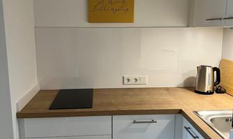 A modern kitchen with white cabinets and a wooden countertop. A yellow picture with writing hangs on the wall.