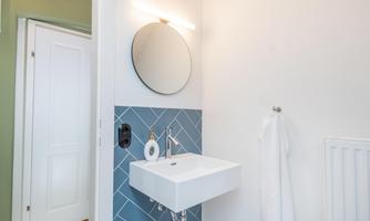 A modern bathroom with a white sink and a round mirror. The wall is adorned with blue tiles.