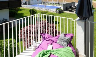 A cozy balcony with a large purple beanbag and a green blanket. In the background, there is a pool and a beautiful landscape with mountains.