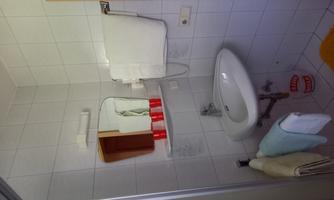 A small bathroom with a sink, a mirror, and towels. Toilet accessories hang on the wall and the floor is covered with a yellow carpet.