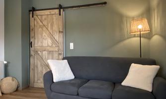 A modern living room with a gray sofa and two white cushions. In the background, there is a wooden sliding door and a soft lamp provides cozy lighting.