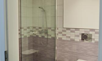 A modern bathroom with shower and toilet. The walls are tiled in soft colors and there is a simple furnishings.