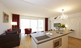 A modern apartment with an open kitchen and a cozy living area. Large windows let in plenty of daylight and offer a pleasant view.