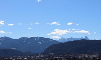An impressive mountain landscape under a clear blue sky. In the foreground, a town is visible, surrounded by majestic mountains.
