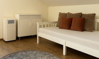 A bright room with a white daybed and two cushions. A wardrobe stands next to the bed and a round rug lies on the floor.