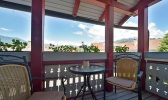 A cozy balcony with two chairs and a small table. In the background, you can see a beautiful landscape with a blue sky and clouds.