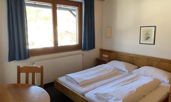 A cozy room with a double bed and wooden details. The window offers a view outside and there is a table with chairs.