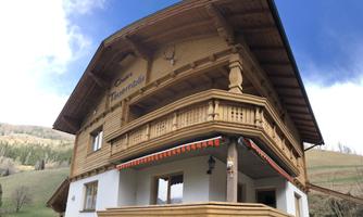 A traditional wooden house with a large balcony and a cozy exterior view. In the background, gentle hills and a blossoming landscape can be seen.