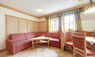 A cozy living space with a red sofa and a wooden table. Large windows let in plenty of day light and create an inviting atmosphere.