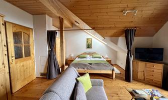 A cozy bedroom with wooden walls and sloping ceilings. There is a double bed, a seating area, and a television.