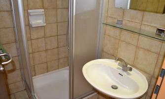 A small bathroom with a shower and a sink. The walls are brightly tiled, and there is a mirror above the sink.