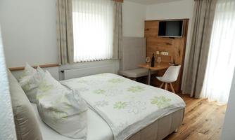 A modern bedroom with a double bed and elegant wooden paneling. A desk and a television complete the furnishings.