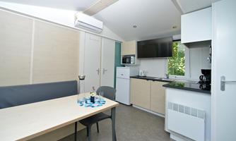 A modern kitchen with a table and chairs. In the background, appliances such as a refrigerator, a microwave, and a television can be seen.