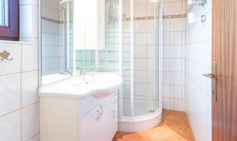 A modern bathroom with a shower and a sink. The floor is tiled, and there is an orange rug on it.