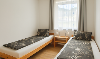 A simple room with two single beds and natural wood frames. The window lets in plenty of daylight and creates a bright atmosphere.