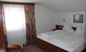 A cozy bedroom with two beds and colorful curtains. A table and a chair are also available, and the room has plenty of natural light.