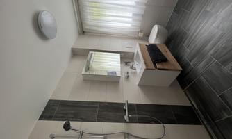 A modern bathroom with a sink, a large mirror, and a shower. The light streams through the curtains, creating a bright, inviting atmosphere.