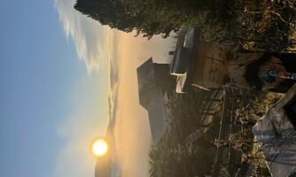 A beautiful sunrise over misty hills with an old wooden house in the background. In the foreground stands a carved statue.