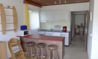 A modern kitchen with a bar area and three barstools. The equipment includes a microwave, a stove, and a refrigerator.