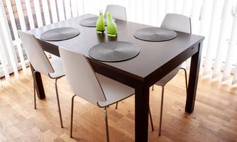 A modern wooden dining table with four white chairs. On the table lie round coasters and two green decorative bottles.