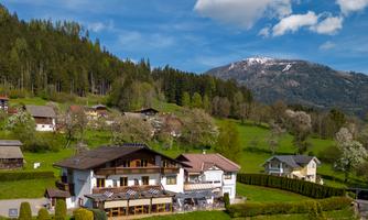 A picturesque house in a green landscape with mountains in the background. The clouds can be seen in the blue sky.