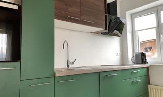 A modern kitchen with green cabinets and a wooden countertop. The window provides plenty of daylight and the kitchen appliances are well placed.