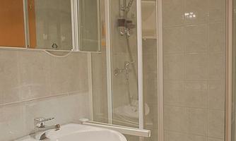 A modern bathroom with a shower and a sink. The walls are tiled in light colors and reflect the light well.