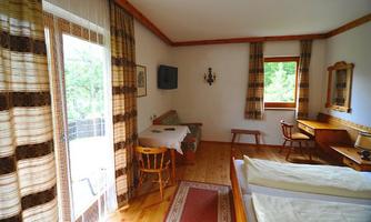 A cozy room with two beds, a table, and chairs. Large windows provide plenty of daylight.