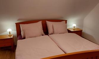 A cozy bedroom with a double bed and bright pillows. Next to the bed are nightstands with table lamps.