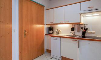 A modern kitchen with white cabinets and wooden details. The kitchen is well-equipped and has a small dining area.
