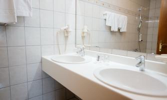 A modern bathroom with two sinks and bright tiles. Towels hang on the wall and a large mirror reflects the space.