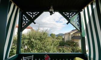 A beautiful view from a covered terrace. In the background, trees and houses can be seen under a cloudy sky.
