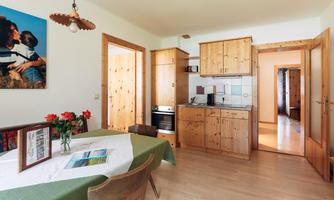 A cozy kitchen with wooden furniture and a dining table. A picture on the wall and fresh flowers give the room an inviting atmosphere.