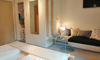 A modern room with two beds and a cozy seating area. A TV hangs on the wall, and there is a large mirror as well as decorative cushions.
