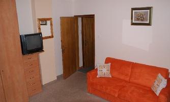 A simple room with an orange sofa and a television. There is also a wooden dresser and a picture on the wall.