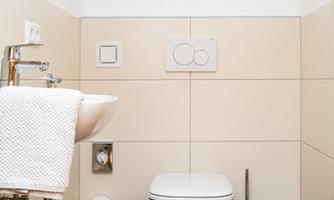A modern bathroom with a toilet and a sink. The walls are tiled in soft colors and the ceiling has wood paneling.