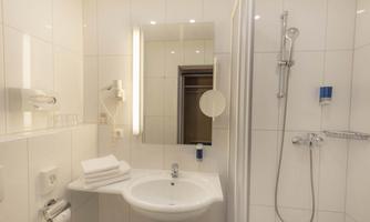 A modern bathroom with clean white tiles. There is a sink, towels, and a shower.