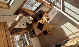 A cozy dining area in a wooden house with a round table and comfortable chairs. Large windows let in plenty of light.