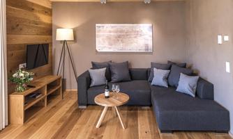 A modernly furnished living room with a cozy couch and hardwood floors. A table with a wine bottle and glasses complements the relaxed atmosphere.