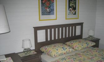 A cozy bedroom with a wooden bed and colorful floral bedding. Two pictures with floral motifs hang on the walls.