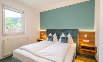 A modern bedroom with a cozy double bed and bright walls. The soft color scheme creates a relaxed atmosphere.