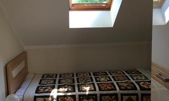 A cozy room with a single bed and a colorful quilt. A skylight lets in a lot of daylight.