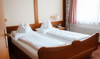 A cozy hotel room with a double bed and two pillows. Large windows provide plenty of daylight.