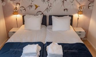 A stylish bedroom with two single beds and cozy pillows. Fresh towels and a lovely wall decoration are placed next to the beds.