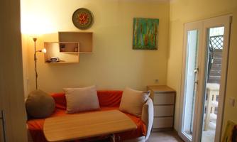 A cozy living space with an orange sofa and a table. The walls are light yellow and there are large windows that let in plenty of light.