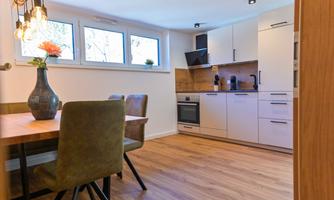 A modern kitchen with a dining table and chairs. Large windows provide plenty of light, and fresh plants create a cozy atmosphere.