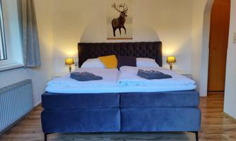 A modern bedroom with a large double bed and soft colors. On the wall hangs a picture of a deer, and there are two nightstands with lamps.