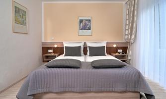 A modern bedroom with a double bed and gray bedding. Large windows provide plenty of light and a relaxed atmosphere.