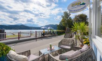 A cozy outdoor area of a café overlooking a lake. Palms and seating invite you to relax.
