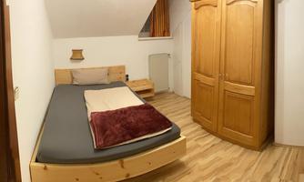 A cozy bedroom with a bed and a television. The room has bright walls and a wooden wardrobe.